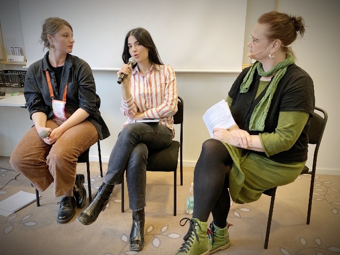 Tre personer sitter på stolar bredvid varandra, varav en har en mikrofon i handen och ser ut att prata. 