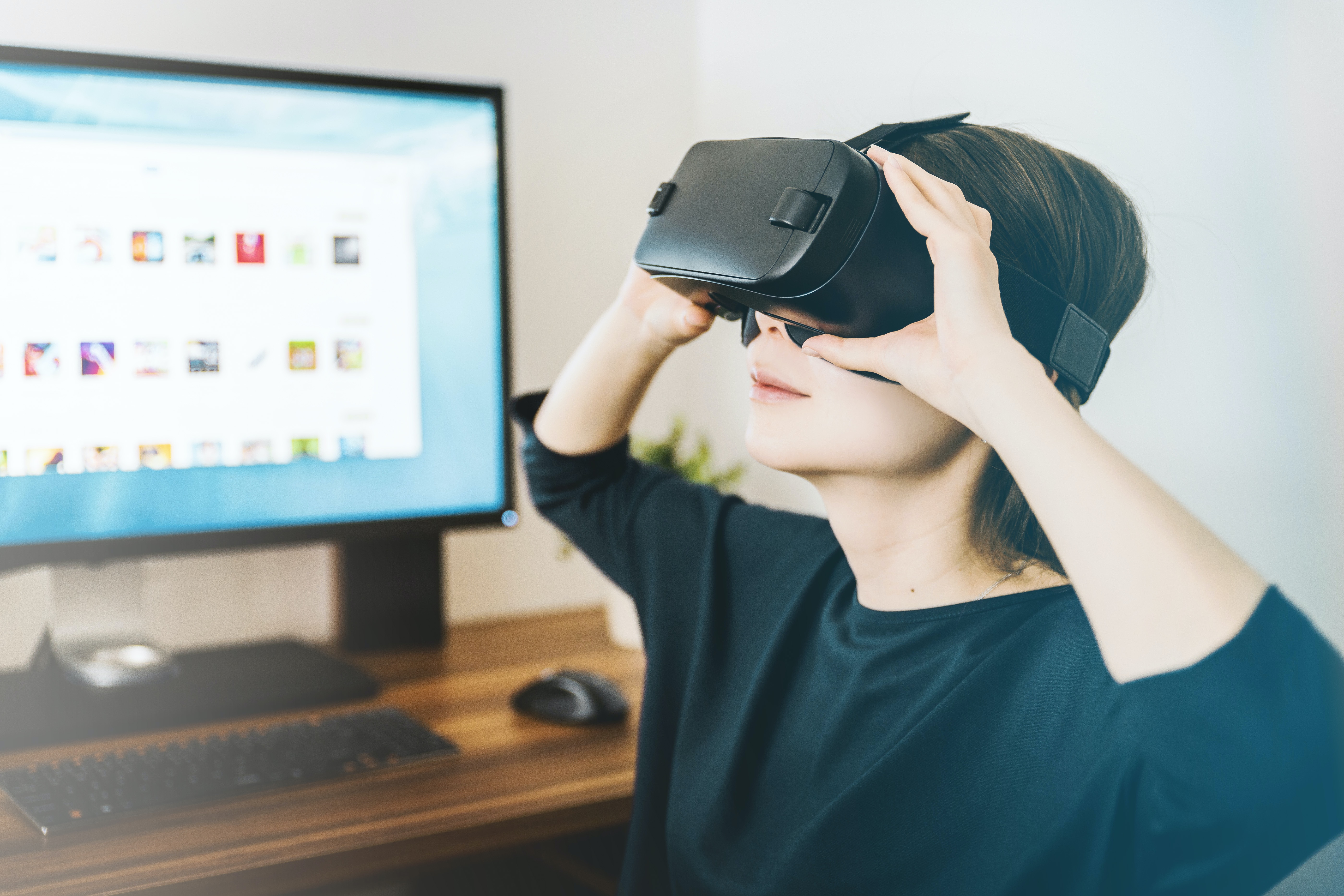 En person håller med sina händer på vr-glasögon som hen har på sig, sittandes framför en dator.