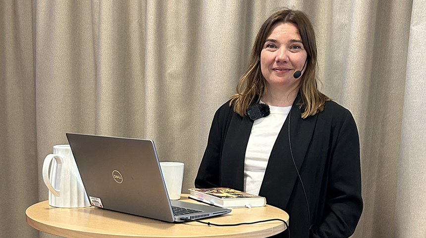Therése Granwald står vid ett ståbord med laptop inför sin föreläsning på infoteket.
