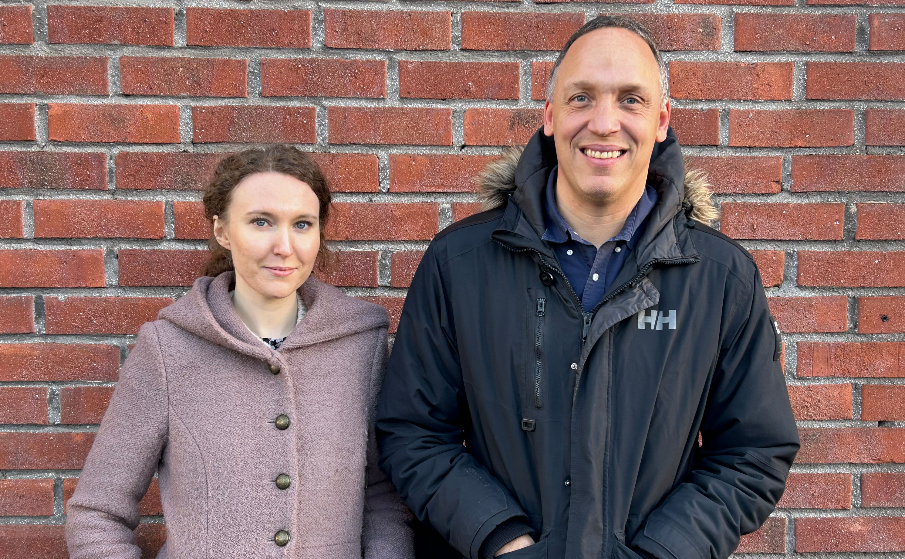 Clara Skogholt och Niklas Rossi utanför infoteket framför den röda tegelväggen.