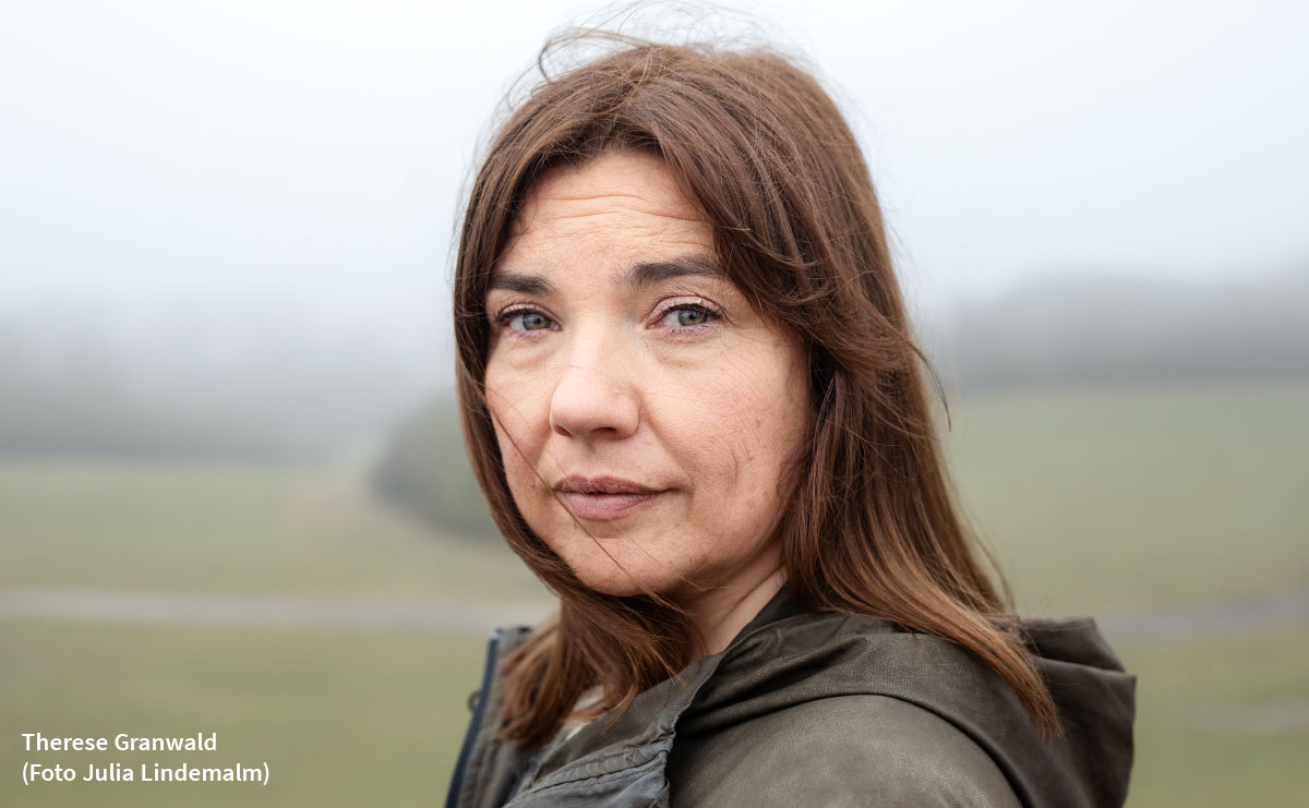 Porträttbild Therese Granwald. Utomhus med gröna fält och skogsdungar i disig bakgrund. Hon ar lång brunt hår och grön jacka med nedfälld huva. Foto: Julia Lindemalm.