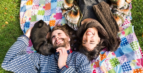 Ett ungt par ligger på en filt och busar med en hundvalp.