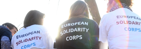 Ungdomar sitter med ryggen mot kameran i tröjor med texten European Solidarity Corps.